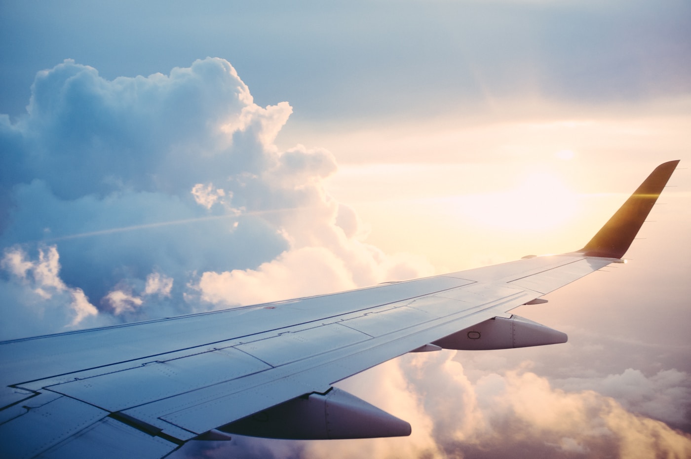 Airplane window view of wing above clouds at sunset